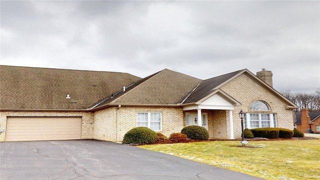 view of front of house featuring an attached garage, brick siding, driveway, a chimney, and a front yard