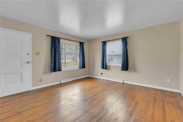 spare room with a baseboard radiator, wood-type flooring, a healthy amount of sunlight, and baseboards