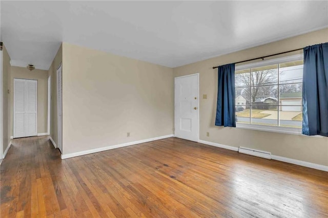 unfurnished room with a baseboard heating unit, baseboards, and hardwood / wood-style flooring