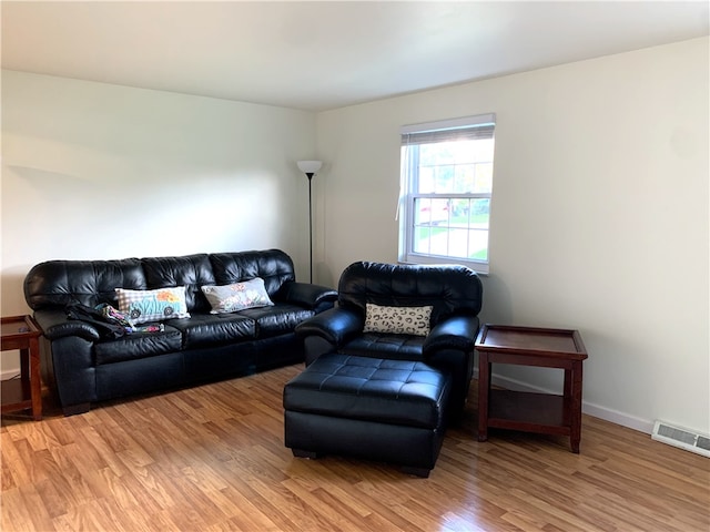 living room with light wood-type flooring, visible vents, and baseboards