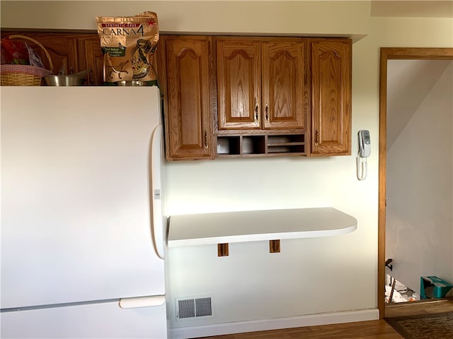 kitchen with brown cabinets, freestanding refrigerator, visible vents, and open shelves