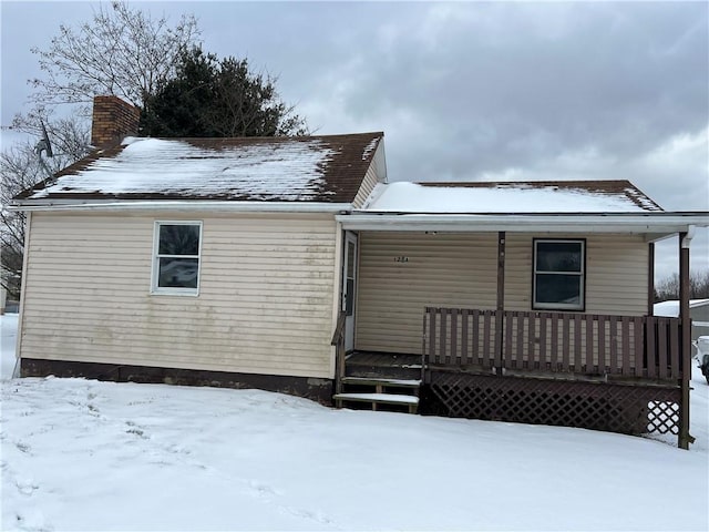 snow covered back of property featuring a chimney