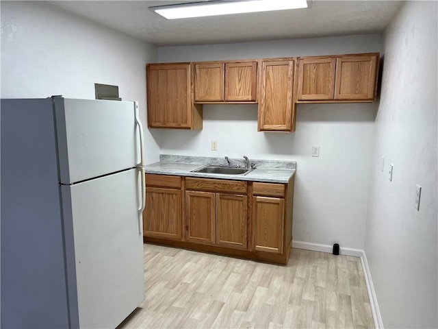 kitchen featuring light countertops, freestanding refrigerator, brown cabinets, and a sink