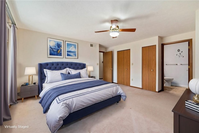 bedroom with connected bathroom, light colored carpet, visible vents, baseboards, and two closets