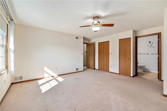 unfurnished bedroom featuring carpet, visible vents, and two closets