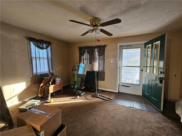 interior space with a ceiling fan, a textured ceiling, baseboards, and a wealth of natural light