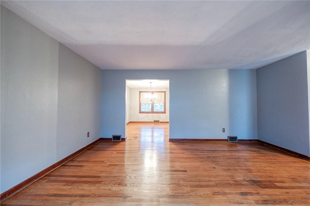 empty room with a chandelier, baseboards, visible vents, and light wood finished floors