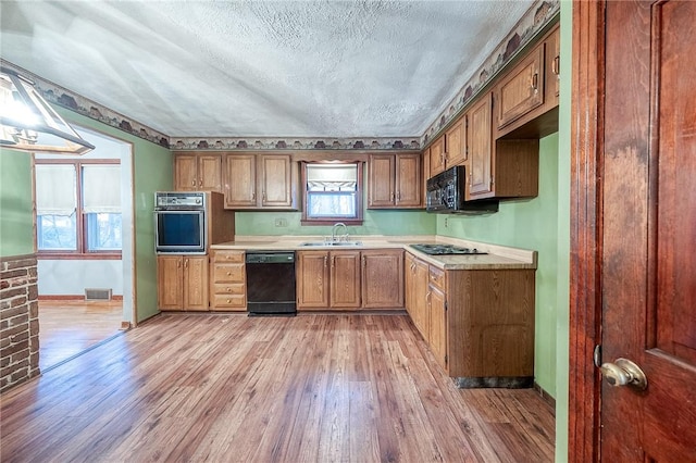 kitchen featuring light countertops, light wood-style flooring, a sink, a textured ceiling, and black appliances