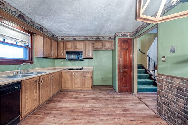 kitchen featuring a sink, light wood-style flooring, black appliances, and a textured ceiling