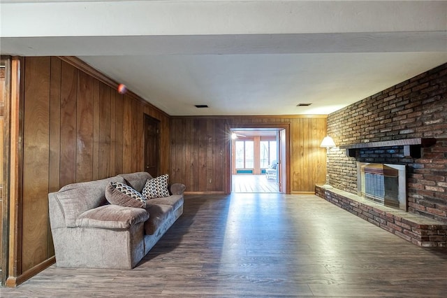 living area featuring a brick fireplace, visible vents, wood finished floors, and wood walls