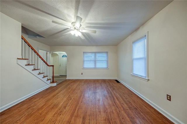 interior space featuring arched walkways, stairway, a textured ceiling, wood finished floors, and baseboards