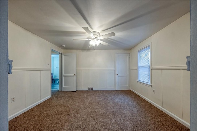 spare room with a ceiling fan, carpet, a wainscoted wall, and visible vents