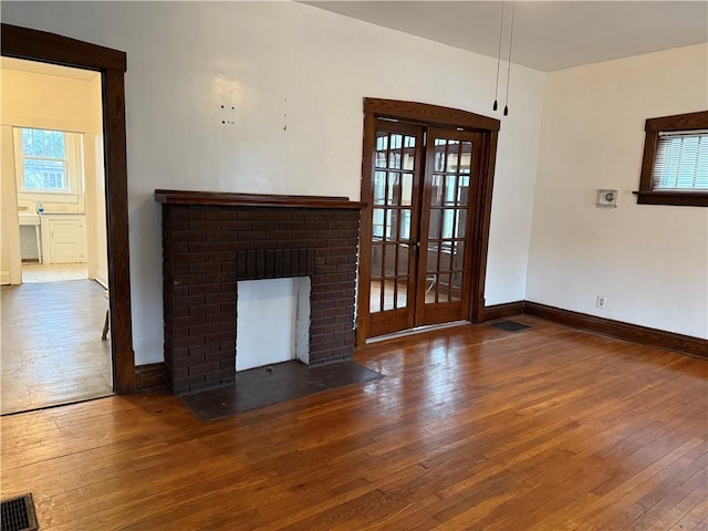 unfurnished living room with baseboards, visible vents, hardwood / wood-style floors, french doors, and a fireplace