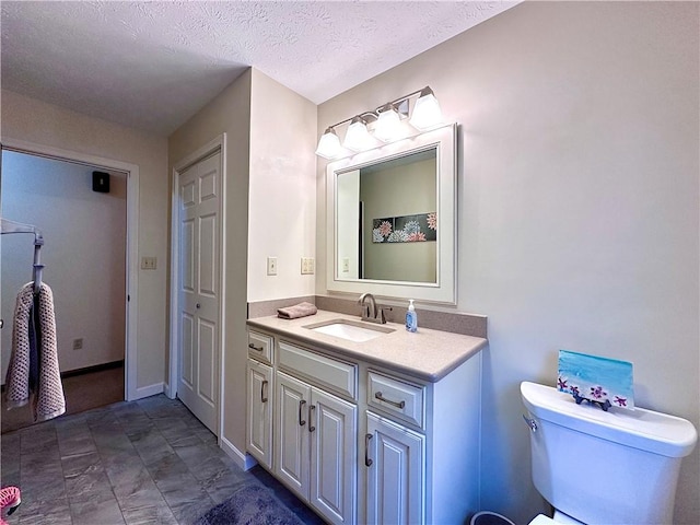 bathroom featuring baseboards, toilet, vanity, and a textured ceiling