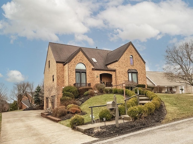 french country home with driveway, roof with shingles, a front lawn, and brick siding