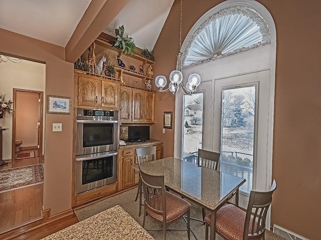 kitchen with brown cabinets, lofted ceiling, double oven, a chandelier, and light wood-type flooring