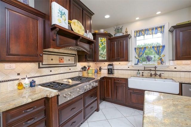 kitchen featuring light tile patterned floors, tasteful backsplash, light stone countertops, stainless steel gas stovetop, and a sink