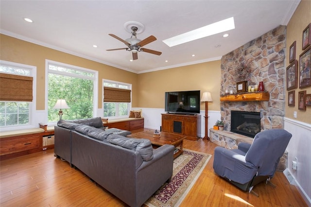 living room with a wainscoted wall, a stone fireplace, wood finished floors, and ornamental molding