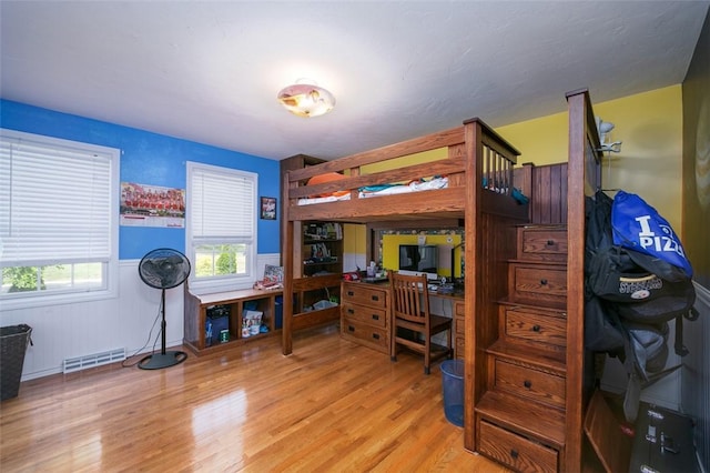 bedroom with a wainscoted wall, multiple windows, visible vents, and light wood-style floors