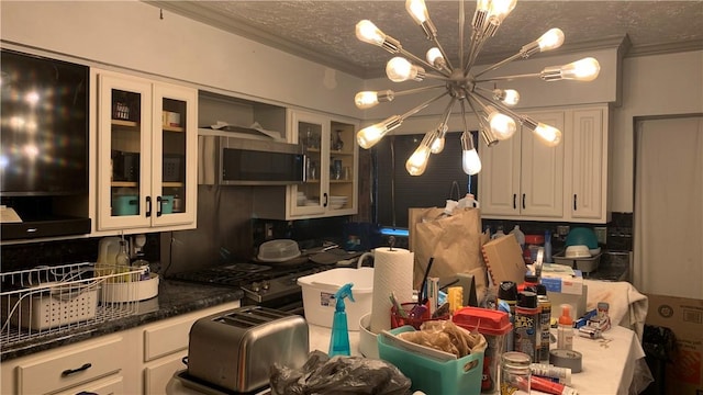 kitchen featuring glass insert cabinets, stainless steel microwave, an inviting chandelier, a textured ceiling, and crown molding