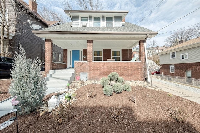 bungalow with roof with shingles, a porch, and brick siding