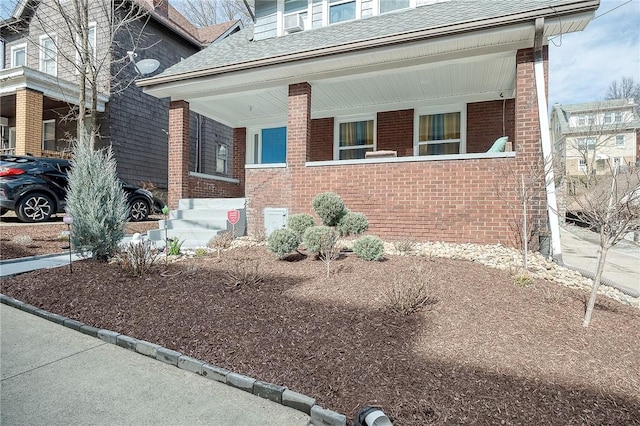 view of front of property with a shingled roof and brick siding