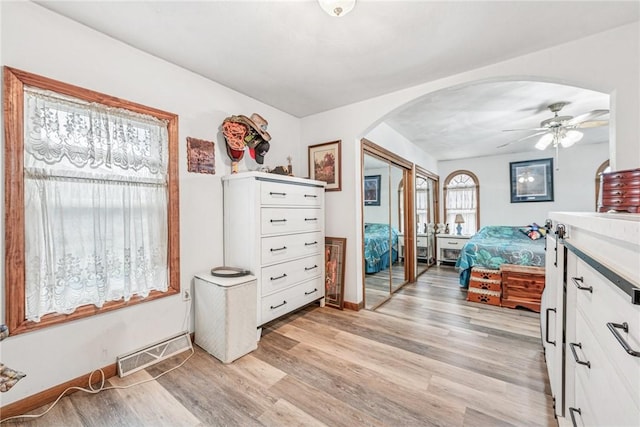 bedroom with arched walkways, a closet, visible vents, light wood-style floors, and a ceiling fan