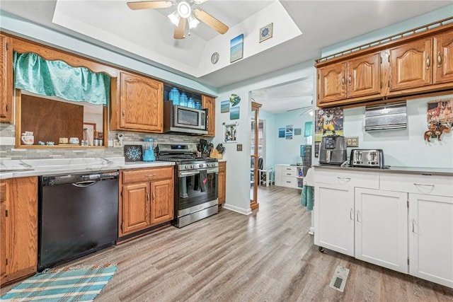 kitchen with appliances with stainless steel finishes, light wood-type flooring, a raised ceiling, and decorative backsplash