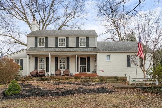 view of front facade with brick siding, covered porch, a chimney, and roof with shingles