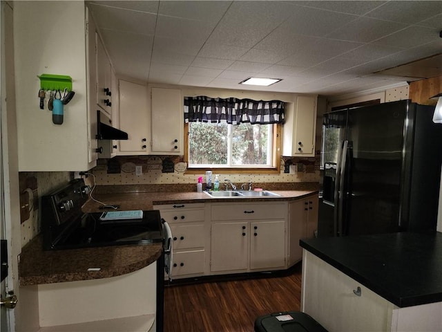 kitchen with dark countertops, white cabinetry, a sink, under cabinet range hood, and black appliances