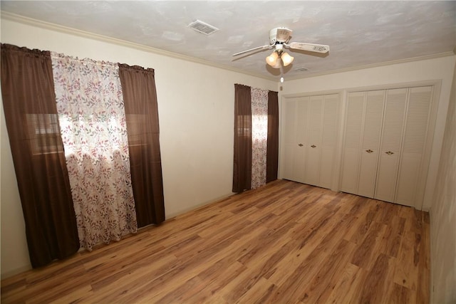 unfurnished bedroom with a ceiling fan, visible vents, multiple closets, light wood-type flooring, and crown molding