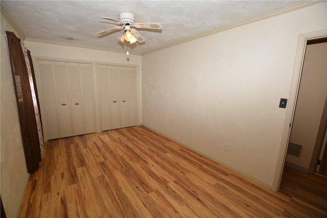 unfurnished bedroom featuring ceiling fan, ornamental molding, two closets, and light wood-style flooring