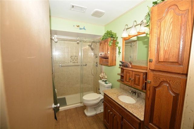 bathroom with visible vents, toilet, vanity, a shower stall, and wood finished floors