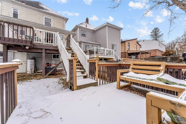 snow covered rear of property with stairway, water heater, and a deck