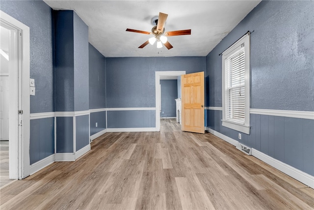 unfurnished room featuring wainscoting, ceiling fan, wood finished floors, and a textured wall