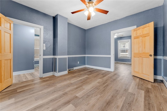 empty room featuring light wood finished floors, baseboards, and a ceiling fan