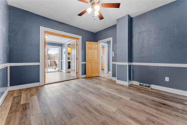 spare room with a wainscoted wall, a textured wall, visible vents, and wood finished floors