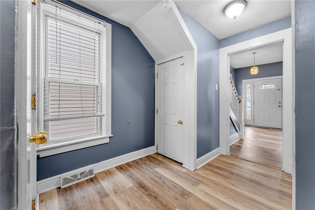 foyer entrance featuring lofted ceiling, baseboards, visible vents, and wood finished floors