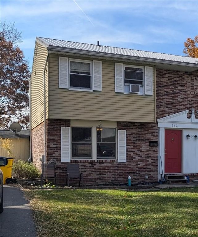 colonial home featuring a front yard, metal roof, and brick siding