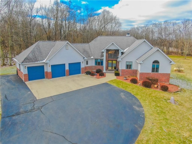 view of front of house featuring aphalt driveway, a garage, brick siding, a front lawn, and a chimney