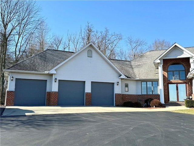 view of front of home featuring driveway, a shingled roof, an attached garage, french doors, and brick siding