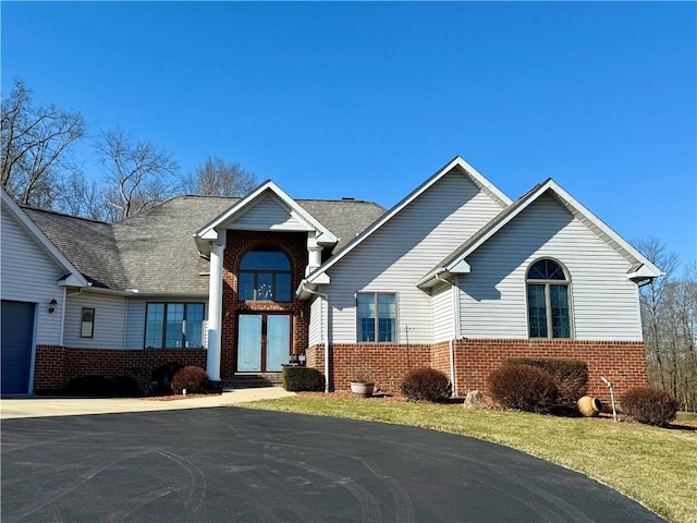 view of front of property featuring aphalt driveway, a front yard, brick siding, and a garage