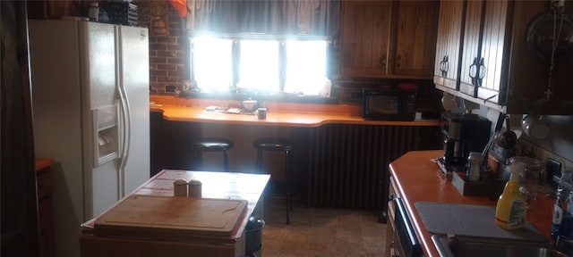 kitchen with black microwave, white refrigerator with ice dispenser, and brown cabinets