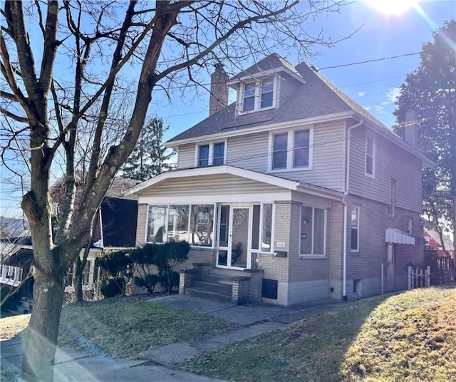 american foursquare style home with a shingled roof, entry steps, a sunroom, and a chimney