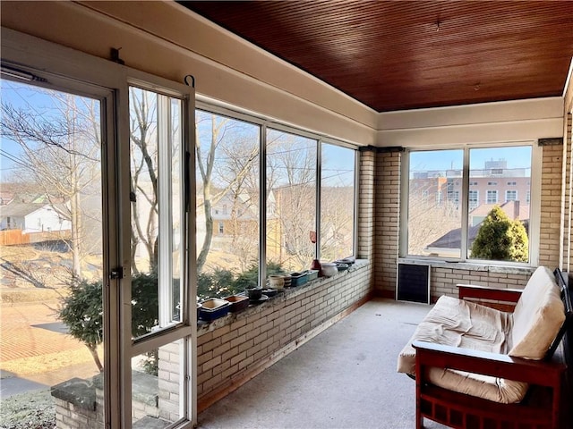 sunroom featuring a healthy amount of sunlight, wooden ceiling, and brick wall