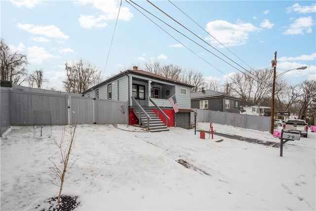 snow covered rear of property with a fenced backyard, stairs, and a chimney