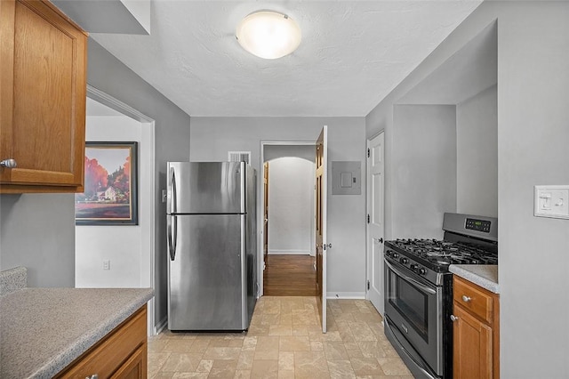 kitchen with appliances with stainless steel finishes, stone finish floor, brown cabinetry, and baseboards