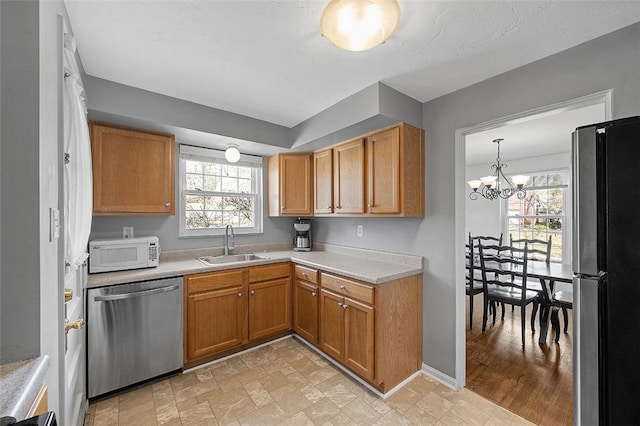 kitchen featuring stainless steel appliances, a sink, light countertops, brown cabinetry, and an inviting chandelier