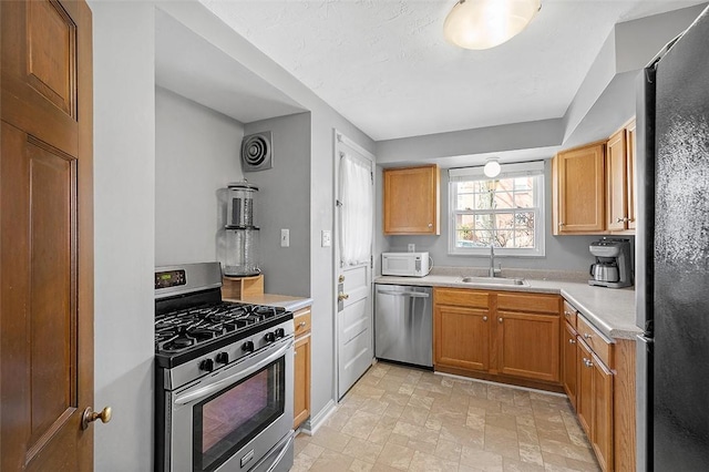 kitchen featuring brown cabinets, stone finish flooring, stainless steel appliances, light countertops, and a sink