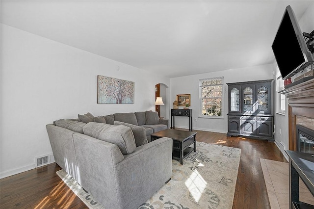 living room with baseboards, visible vents, arched walkways, a fireplace with flush hearth, and wood finished floors